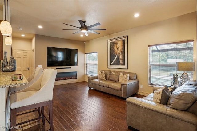 living room featuring baseboards, a glass covered fireplace, dark wood finished floors, and recessed lighting