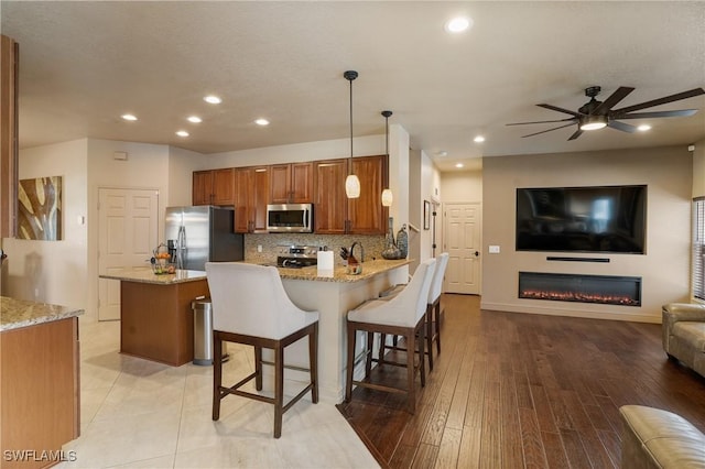 kitchen featuring light stone counters, a breakfast bar area, a peninsula, appliances with stainless steel finishes, and decorative light fixtures