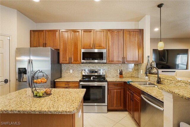 kitchen with light stone countertops, stainless steel appliances, a sink, hanging light fixtures, and brown cabinets