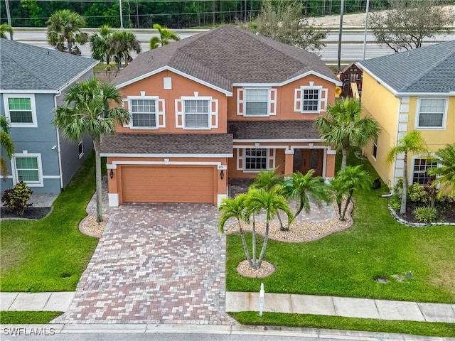 traditional-style house with a garage, a shingled roof, decorative driveway, and stucco siding