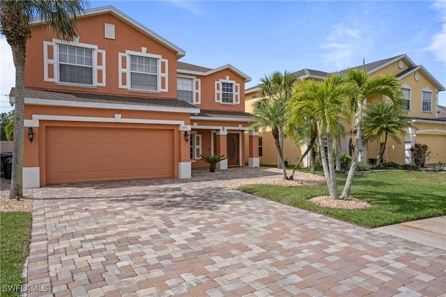 view of front facade featuring a front yard, decorative driveway, an attached garage, and stucco siding