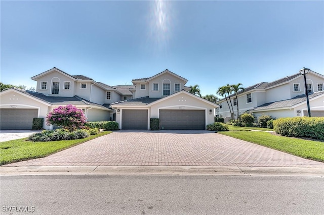 traditional-style home featuring a front yard, decorative driveway, an attached garage, and stucco siding