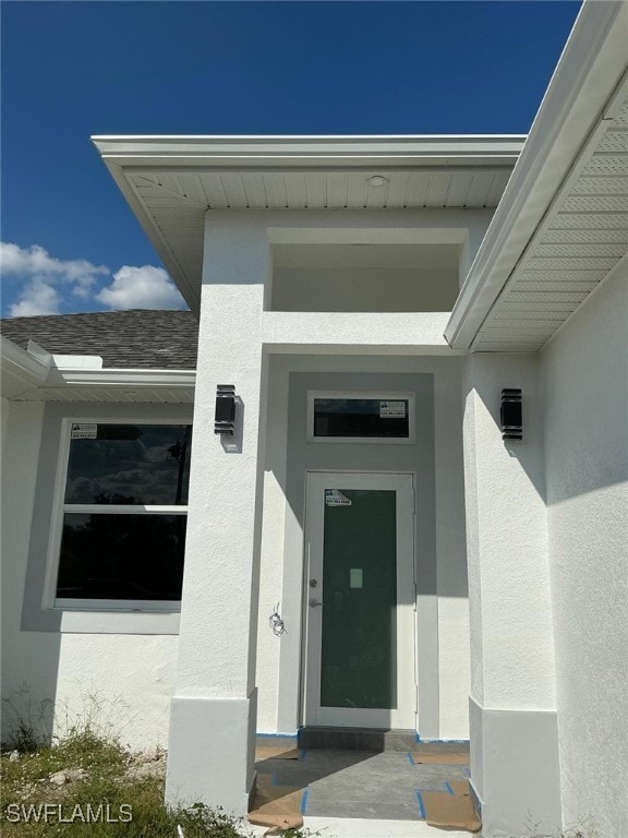 doorway to property featuring roof with shingles and stucco siding