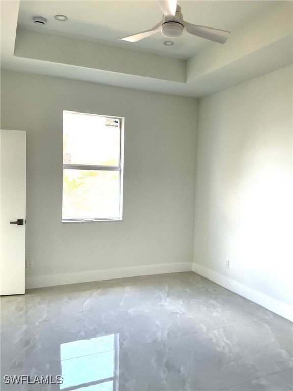 spare room with a raised ceiling, ceiling fan, and baseboards