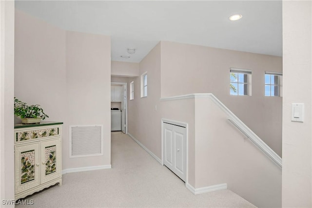 hall with light carpet, baseboards, visible vents, washer / clothes dryer, and an upstairs landing