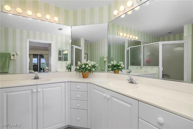 bathroom featuring double vanity, a stall shower, a sink, and wallpapered walls