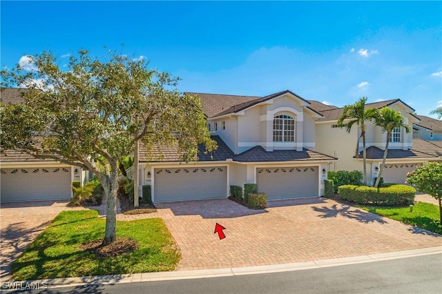 view of front of house with decorative driveway, an attached garage, and stucco siding