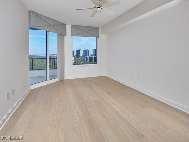 spare room with baseboards, a city view, a ceiling fan, and light wood-style floors