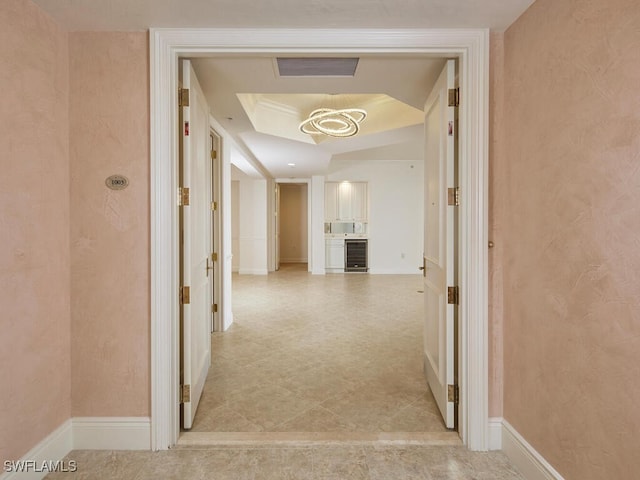 hallway featuring a tray ceiling, beverage cooler, visible vents, and baseboards