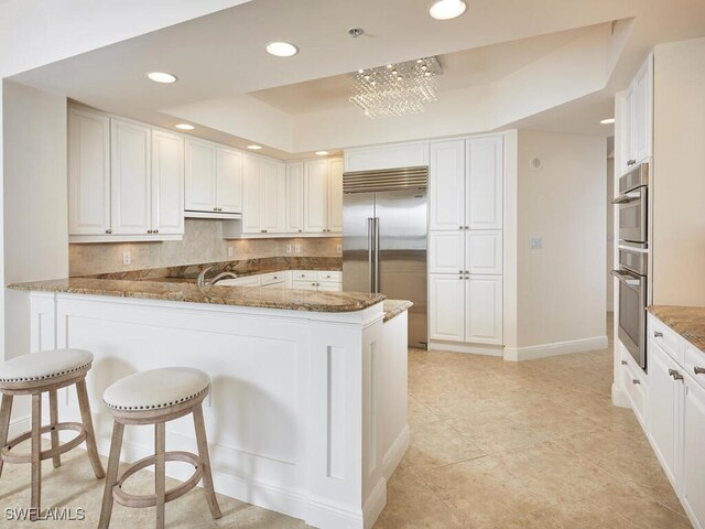 kitchen featuring a peninsula, stone countertops, a raised ceiling, and stainless steel built in fridge