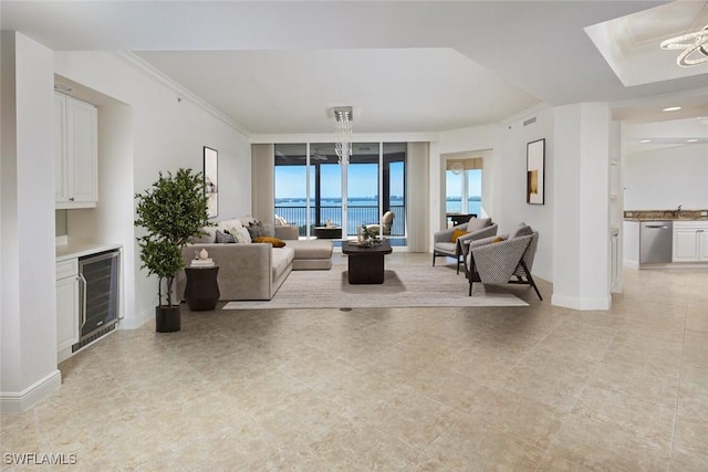 living room featuring baseboards, indoor bar, wine cooler, crown molding, and a notable chandelier