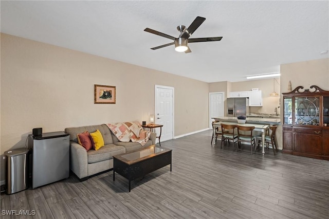 living area with dark wood-style flooring, ceiling fan, and baseboards