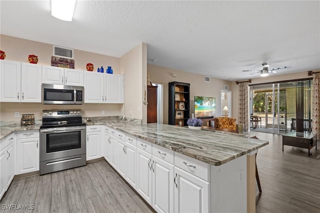 kitchen with visible vents, appliances with stainless steel finishes, white cabinetry, a peninsula, and a kitchen breakfast bar