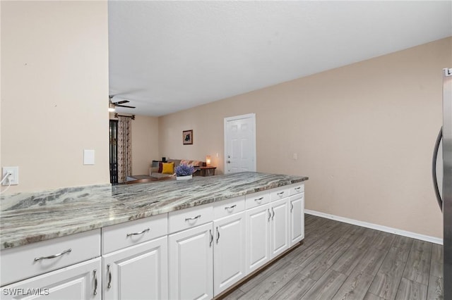 kitchen with light stone counters, open floor plan, wood finished floors, a peninsula, and white cabinetry