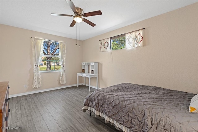 bedroom featuring a ceiling fan, multiple windows, baseboards, and wood finished floors