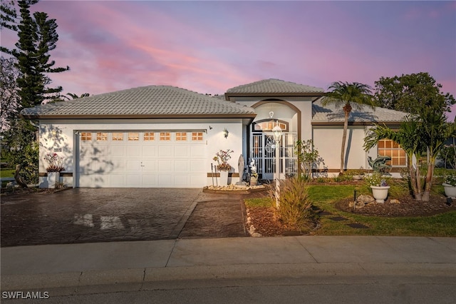 view of front of property featuring a garage, decorative driveway, a tile roof, and stucco siding