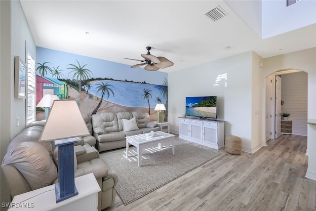 living room with arched walkways, a ceiling fan, baseboards, visible vents, and light wood-style floors