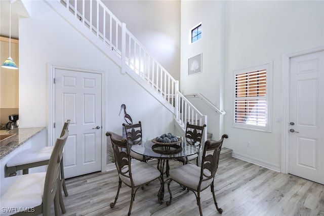 dining area featuring light wood finished floors, baseboards, a high ceiling, and stairway