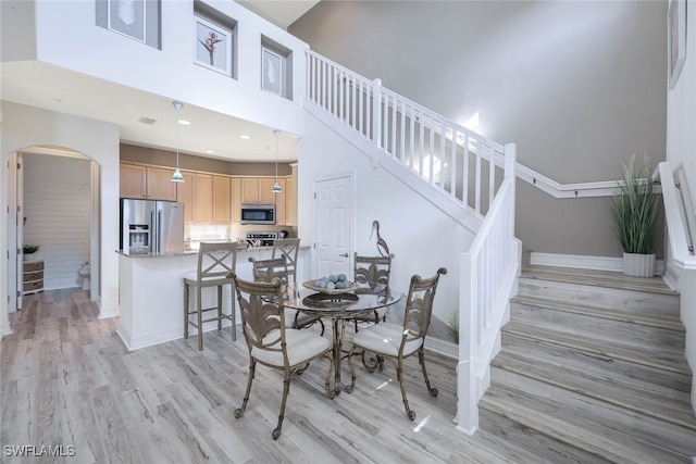 dining area with light wood finished floors, baseboards, arched walkways, a towering ceiling, and stairs