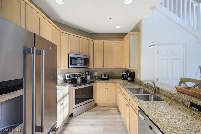 kitchen featuring appliances with stainless steel finishes, light stone countertops, light brown cabinetry, light wood-type flooring, and a sink