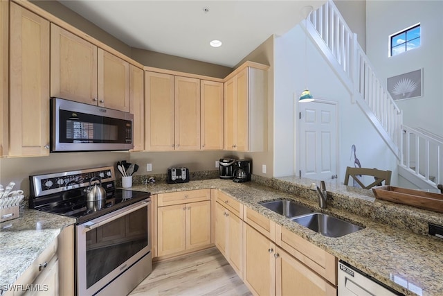 kitchen featuring stainless steel appliances, light brown cabinets, a sink, and light stone counters