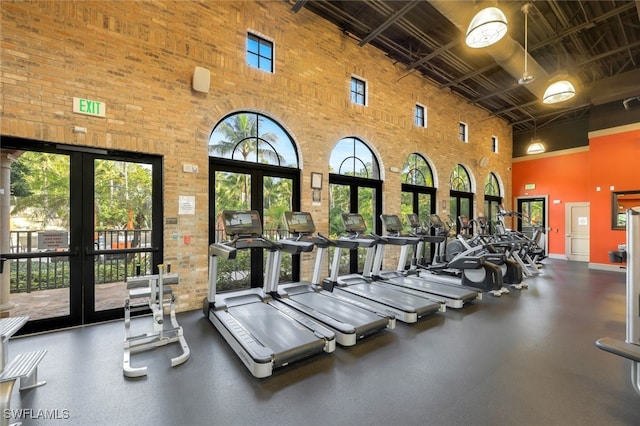 gym with french doors, a towering ceiling, and a healthy amount of sunlight