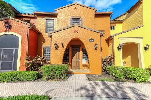 view of exterior entry with a tiled roof, a porch, and stucco siding