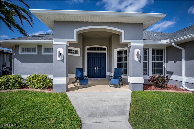 doorway to property featuring roof with shingles, a yard, and stucco siding