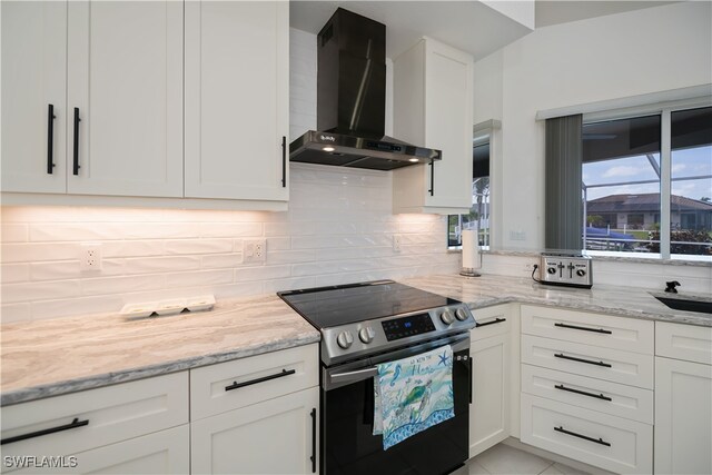 kitchen with decorative backsplash, light stone counters, stainless steel electric range, wall chimney range hood, and white cabinetry