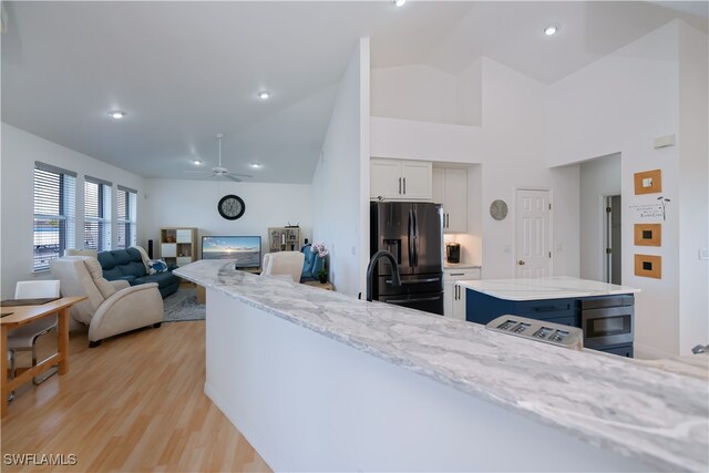 kitchen with black fridge with ice dispenser, a ceiling fan, white cabinets, light stone countertops, and light wood-type flooring