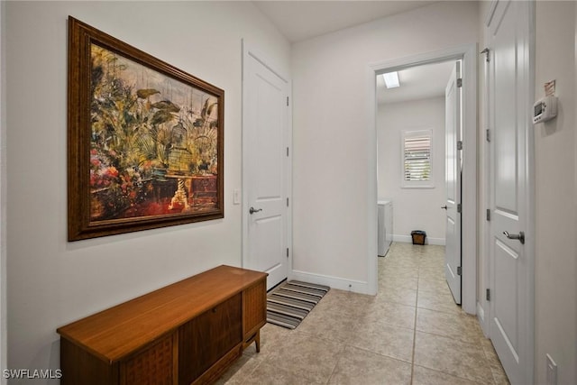 hall featuring light tile patterned floors, washing machine and clothes dryer, and baseboards