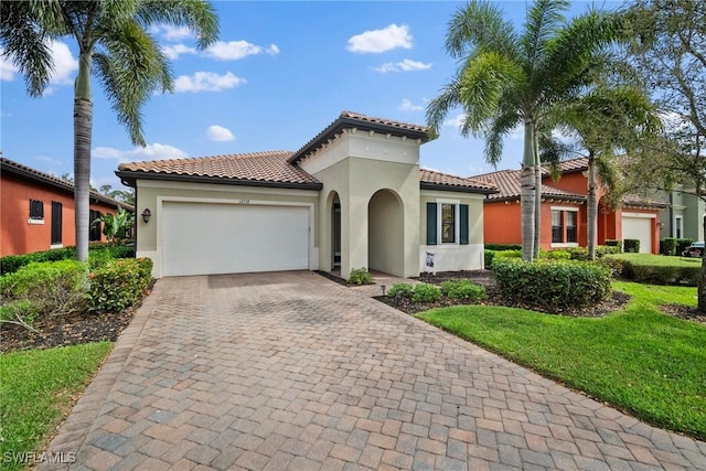 mediterranean / spanish home featuring decorative driveway, a tile roof, stucco siding, an attached garage, and a front lawn