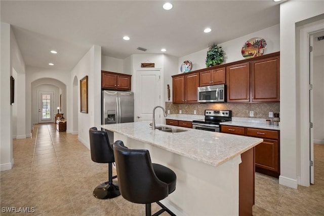 kitchen featuring tasteful backsplash, a center island with sink, appliances with stainless steel finishes, a kitchen breakfast bar, and a sink