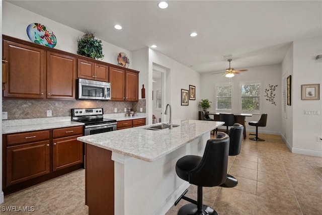 kitchen with a breakfast bar area, a sink, appliances with stainless steel finishes, tasteful backsplash, and an island with sink