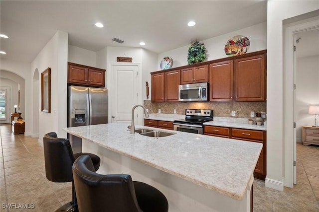 kitchen with arched walkways, appliances with stainless steel finishes, a kitchen breakfast bar, a kitchen island with sink, and a sink