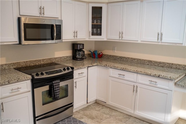 kitchen with white cabinets, glass insert cabinets, stainless steel appliances, and light stone counters