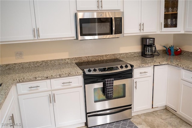 kitchen featuring stainless steel appliances, light stone counters, glass insert cabinets, and white cabinetry