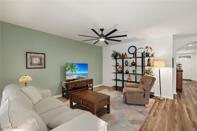 living room with arched walkways, baseboards, a ceiling fan, and light wood-style floors