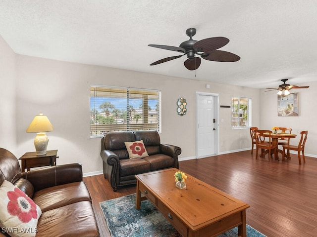 living room with ceiling fan, a textured ceiling, baseboards, and wood finished floors