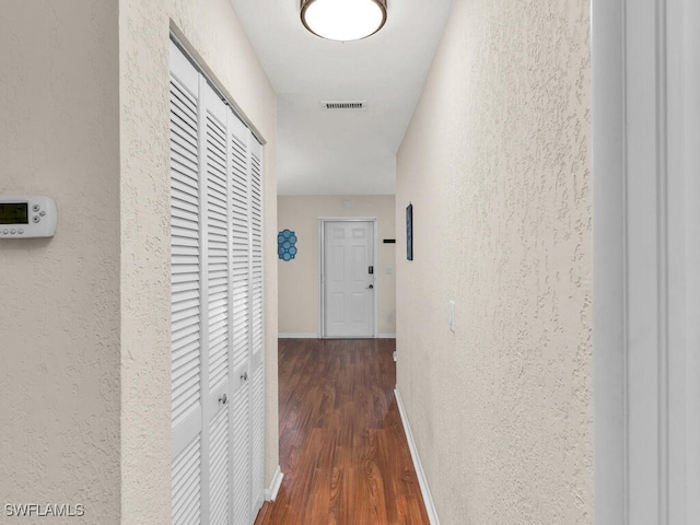 hall with a textured wall, wood finished floors, visible vents, and baseboards