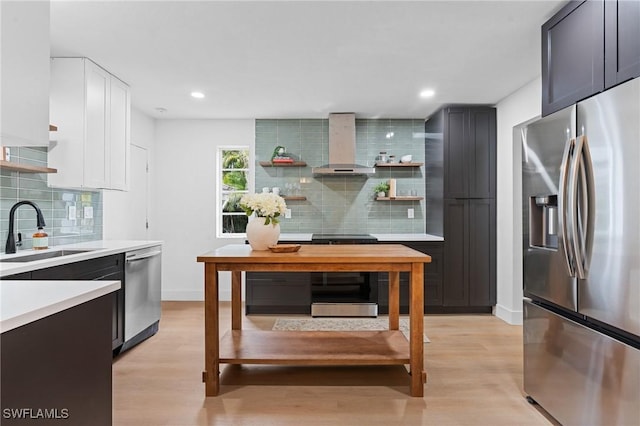 kitchen with open shelves, light countertops, appliances with stainless steel finishes, a sink, and wall chimney exhaust hood