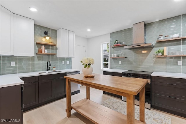 kitchen with light countertops, wall chimney range hood, white cabinetry, a sink, and range with electric stovetop