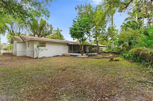 rear view of property featuring a sunroom, fence, and stucco siding