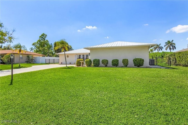 view of front of house featuring metal roof, fence, a front lawn, and stucco siding