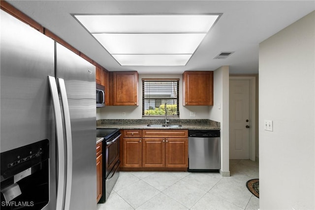 kitchen featuring stainless steel appliances, dark countertops, brown cabinetry, light tile patterned flooring, and a sink