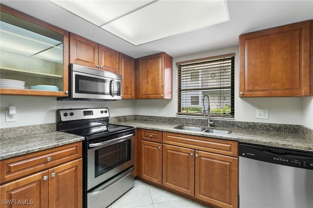 kitchen featuring stainless steel appliances, brown cabinetry, a sink, and light tile patterned floors