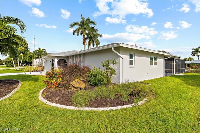 view of property exterior featuring a sunroom, a lawn, an attached garage, and stucco siding