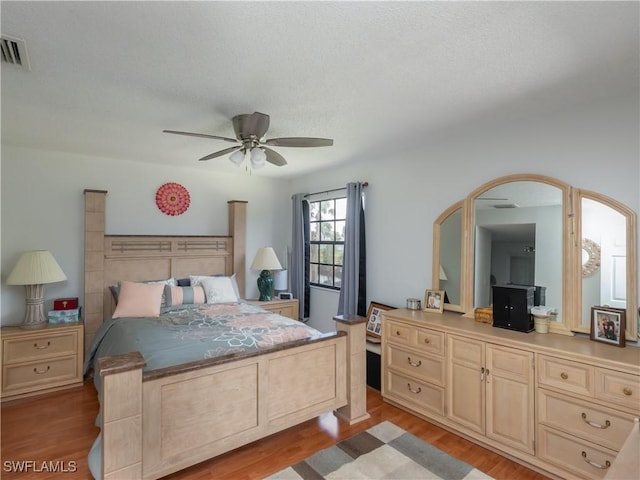 bedroom with light wood finished floors, a textured ceiling, visible vents, and a ceiling fan