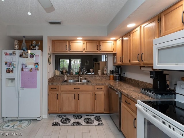 kitchen with a textured ceiling, white appliances, a sink, visible vents, and dark countertops