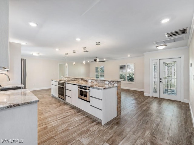 kitchen featuring oven, visible vents, white cabinetry, and a sink